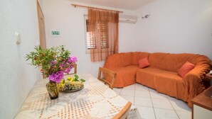 A small living room with a sofa, a table with a vase of flowers, and a window with curtains. - Apartments Longo - Standard One Bedroom Apartment with Terrace(A3) (Supetar)