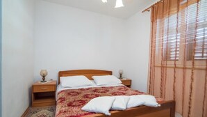 A neatly made bed with a patterned bedspread, two bedside tables with lamps, and a window with curtains. - Apartments Longo - Standard One Bedroom Apartment with Terrace(A3) (Supetar)