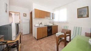 Une cuisine compacte avec des meubles en bois, un réfrigérateur, une cuisinière et un coin repas comprenant une table verte et des chaises à rayures.