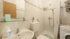 Une salle de bain équipée d’un lavabo, d’un miroir, d’une douche et d’un lave-linge.