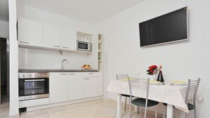 Eine moderne Küche mit weißen Schränken, einem eingebauten Backofen und einer Mikrowelle. Es gibt einen Esstisch mit Stühlen und einen flachbildschirmfernseher an der Wand.