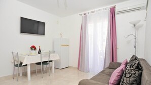 Ein modernes Wohnzimmer mit einer Couch, einem Esstisch mit Stühlen, einem an der Wand montierten Flachbildfernseher und einem Kühlschrank.