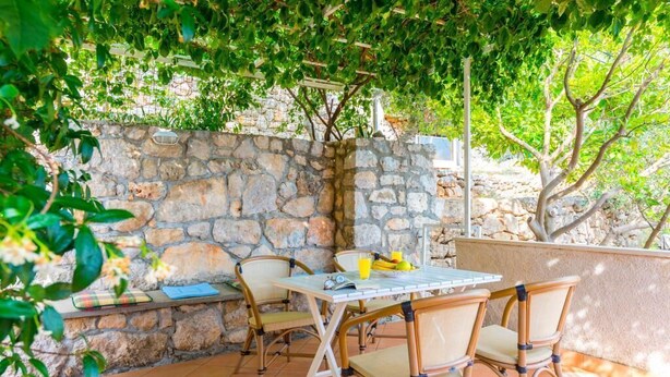 Un patio al aire libre con pared de piedra, sillas de mimbre y una mesa lista para dos.