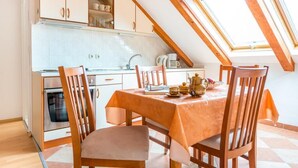 Un comedor con una mesa dispuesta para cuatro, sillas de madera, una cocina al fondo y un tragaluz arriba.