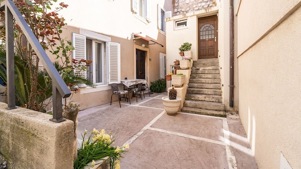 A narrow courtyard with a stone staircase, outdoor seating, and potted plants.