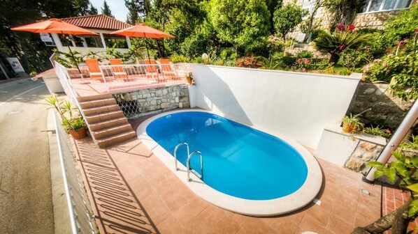 Ein Pool mit Steinmauer, Treppe und Sitzgelegenheiten mit Sonnenschirmen.