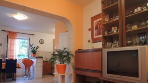 Uma sala de estar com televisão, um espaço de jantar com mesa e cadeiras, e uma cozinha ao fundo.
