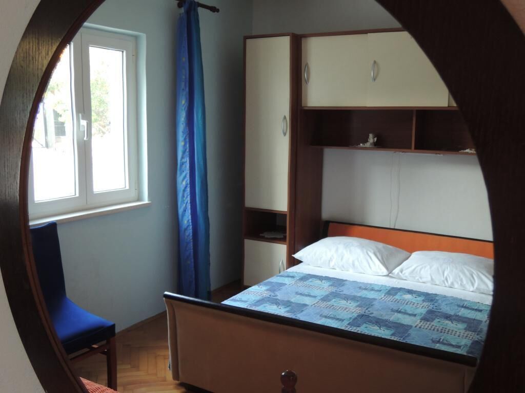 A bedroom with a bed, a chair, a wardrobe, and a window with curtains.