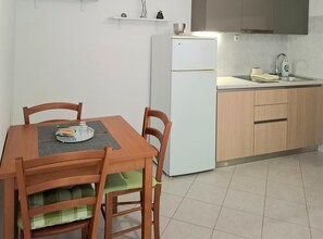 Cozinha compacta com geladeira branca, armários de madeira, pia e mesa de jantar com cadeiras.