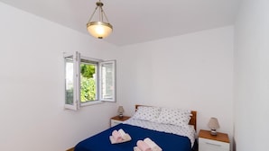 Un dormitorio con una cama, dos mesitas de noche, un ventanal y una lámpara colgante.