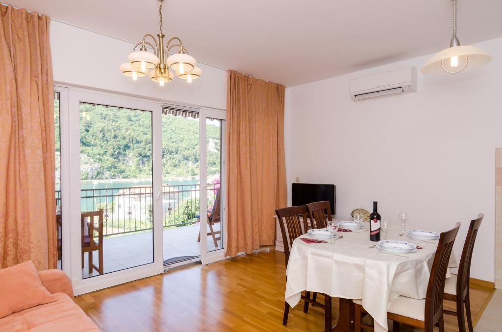 Ein Essbereich mit Tisch für vier Personen, einer Couch und einem Balkon mit Blick auf Grünflächen.