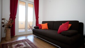 A living room with a dark brown sofa, red and orange cushions, a patterned rug, and a vase with dried flowers. - Apartments Briest (Dubrovnik)