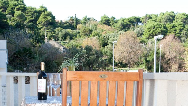 A wooden chair and table set on a tiled patio with a bottle of wine and a glass. - Apartments Briest (Dubrovnik)
