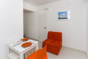 A small, bright room with a white table set for two, a single orange chair, and a door. - Apartments Posta - Comfort One-Bedroom Apartment with Terrace and Sea View (Saplunara)