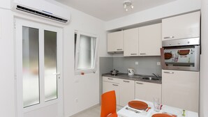 Eine moderne Küche mit weißen Schränken, einem eingebauten Backofen und einem Essbereich mit orangefarbenen Stühlen und einem weißen Tisch.