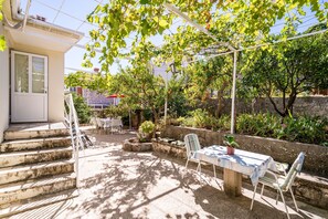 A patio area with a table and chairs, surrounded by greenery and a stone wall.