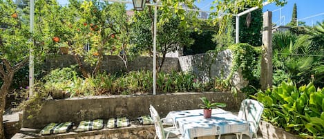 Un patio al aire libre con una mesa y sillas, rodeado de abundante vegetación y un muro de piedra.