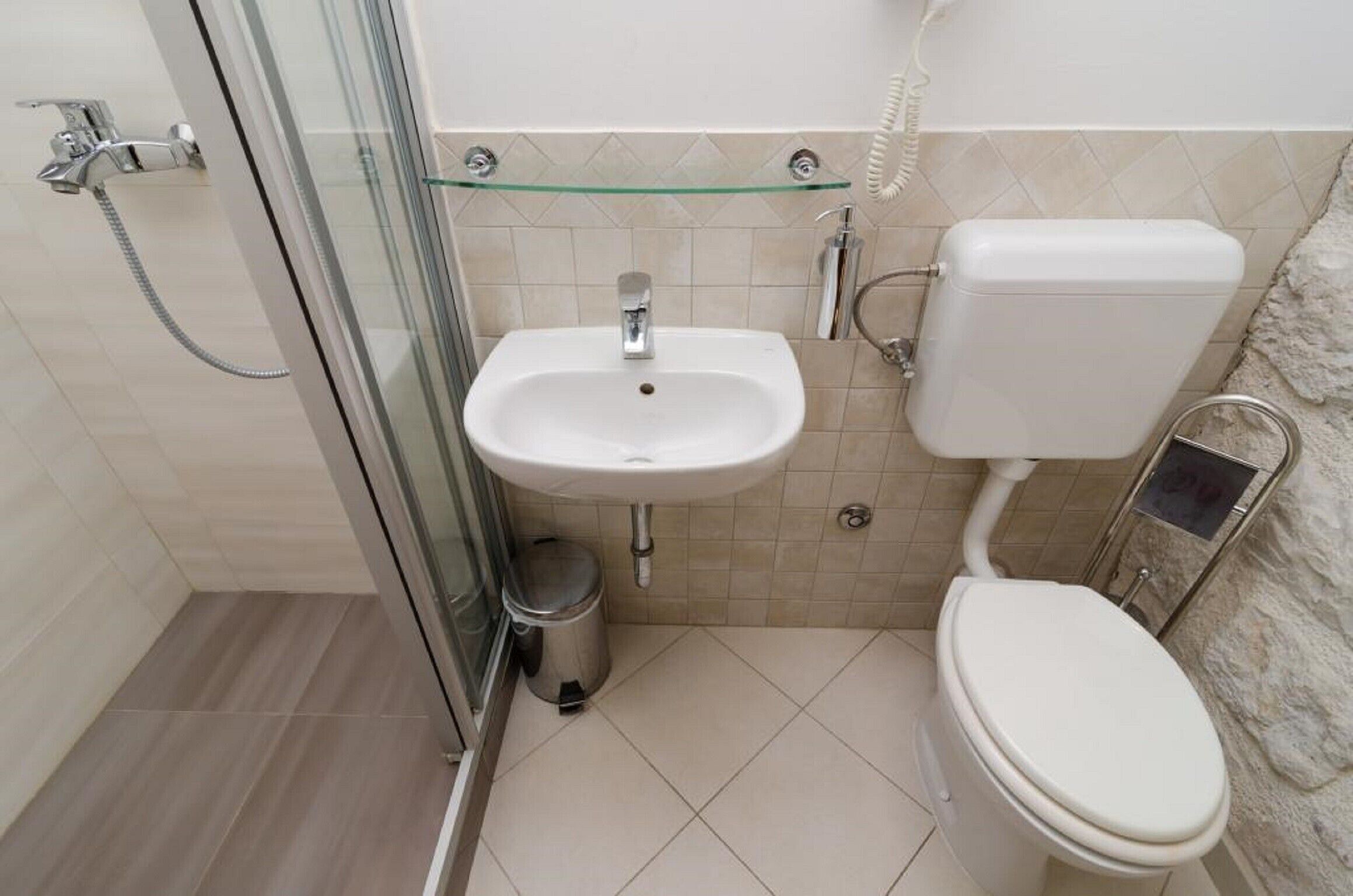 Ein Badezimmer mit Duschkabine aus Glas, Waschbecken in Weiß, Toilette und Mülleimer.