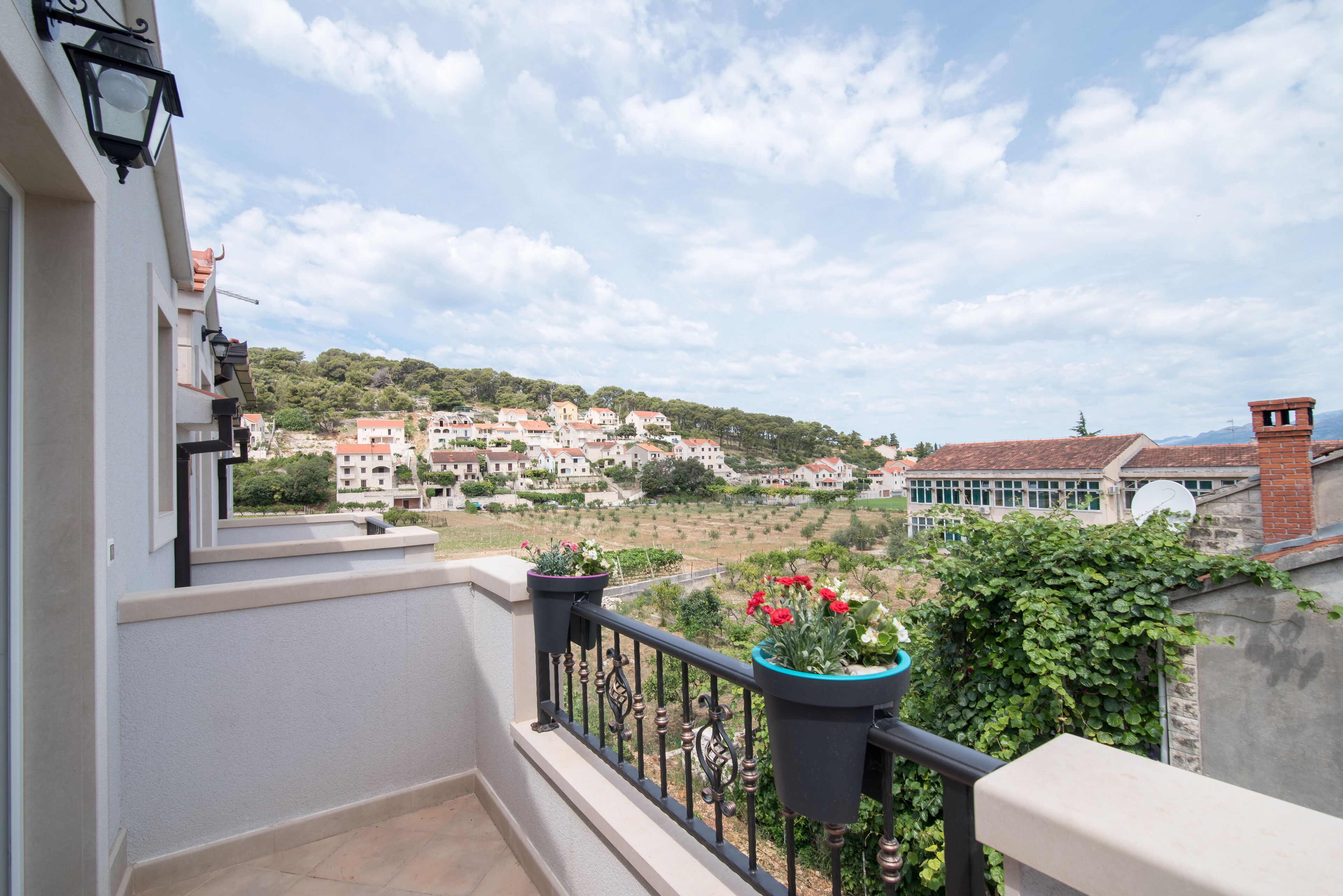 A balcony with potted plants and a view of a hillside town.