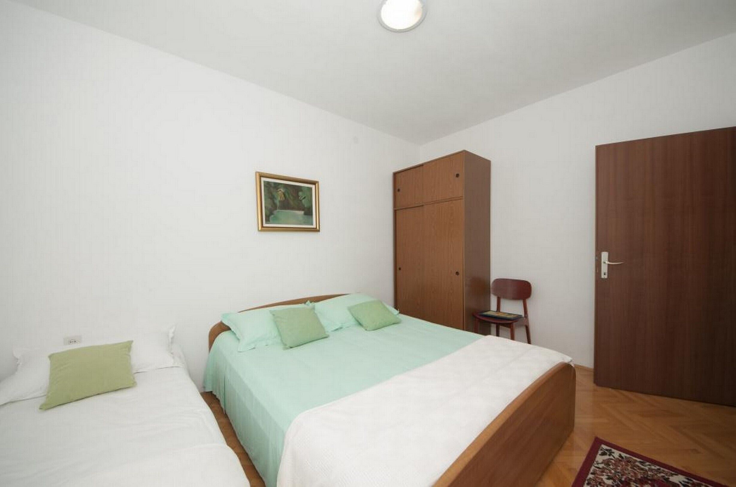 Ein Schlafzimmer mit zwei Betten, einem Kleiderschrank, einem Stuhl und einem gerahmten Bild an der Wand.