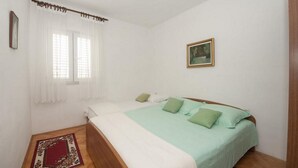 Una camera da letto con un letto, una finestra con tende bianche, un quadro appeso al muro e un tappeto rosso e verde sul pavimento.