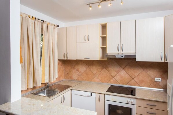 A kitchen with light-colored cabinets, a double sink, a dishwasher, an oven, and a tiled backsplash.