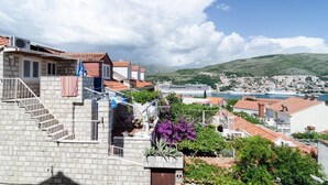 Un pueblo costero con edificios de piedra, una escalera que lleva a una terraza y vistas al mar y colinas lejanas.