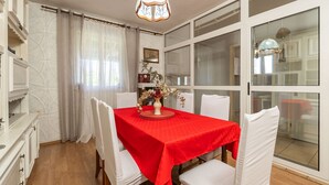 A dining area with a red tablecloth, white chairs, a vase with flowers, and a chandelier.