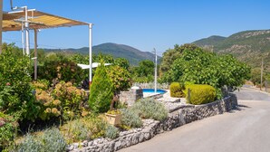A rural road with a stone wall, a blue swimming pool, and lush greenery.