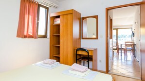 Une pièce comprenant une armoire en bois, un bureau avec une chaise, une table avec des serviettes et un miroir au mur.