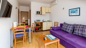 Un espace de vie compact comprenant une cuisine, un coin repas et un canapé violet.