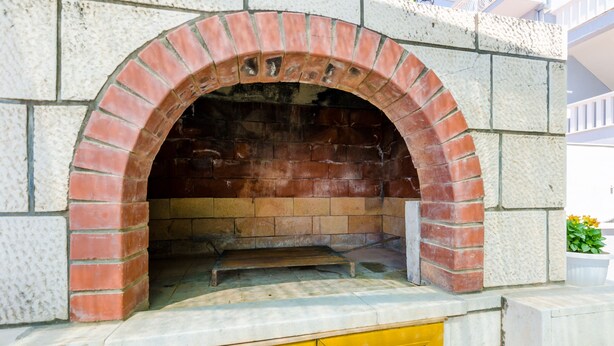 Una chimenea de ladrillo integrada en una pared de piedra, con una puerta amarilla debajo.