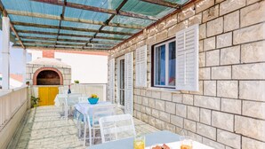 Un patio al aire libre cubierto con suelo de piedra, muebles blancos, pared de piedra y un horno de ladrillo.