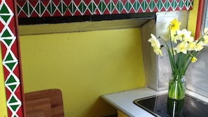 A kitchen with a yellow wall, a wooden cabinet with a red door, a white countertop, and a vase with yellow flowers. - Rumenco, self contained 2 person, secluded/unique off grid glamping, own meadow! (boncath)