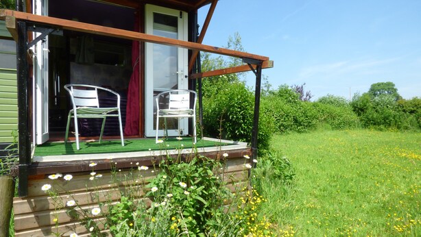 A wooden house with a porch, two white chairs, and a green lawn with yellow flowers. - Rumenco, self contained 2 person, secluded/unique off grid glamping, own meadow! (boncath)