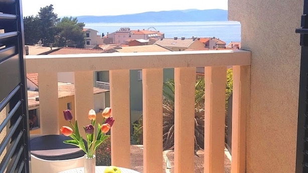 A balcony with a view of the sea, a small table with a vase of flowers, and a chair.