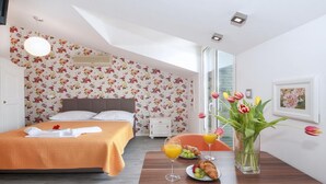 A bedroom with a bed, a nightstand, a bedside table with a glass of orange juice, a plate of food, and a vase with flowers.