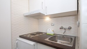 A compact kitchenette with a stove, sink, and white cabinets.