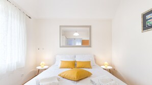 A neatly made bed with white and yellow bedding, two bedside lamps, and a mirror above the bed.