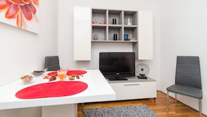 Una sala de estar moderna con un mueble blanco para televisor, un televisor de pantalla plana, un sofá gris y una mesa de comedor con individuales rojos.