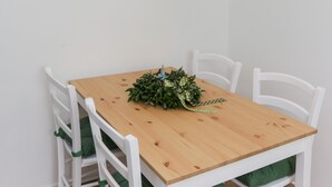 Un'area pranzo con un tavolo in legno, sedie bianche con cuscini verdi, una lampada a sospensione e un quadro appeso al muro.