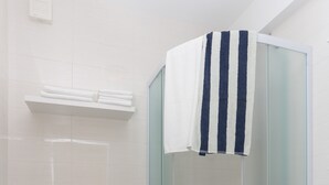Un bagno moderno con doccia vetro, water bianca e tappeto a righe sul pavimento.