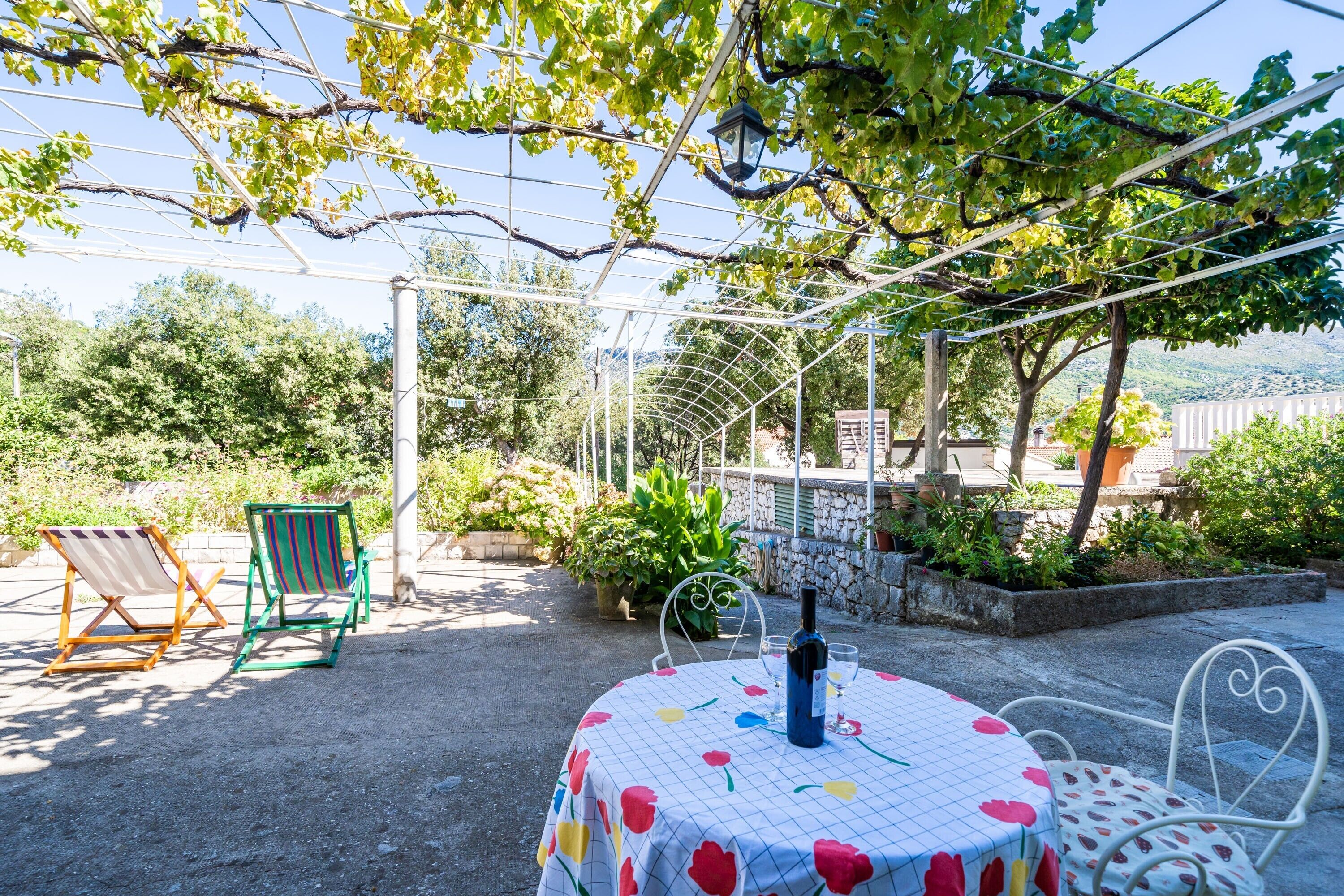Une terrasse extérieure avec une table dressée pour deux personnes, entourée de chaises en métal et surmontée d’une pergola.