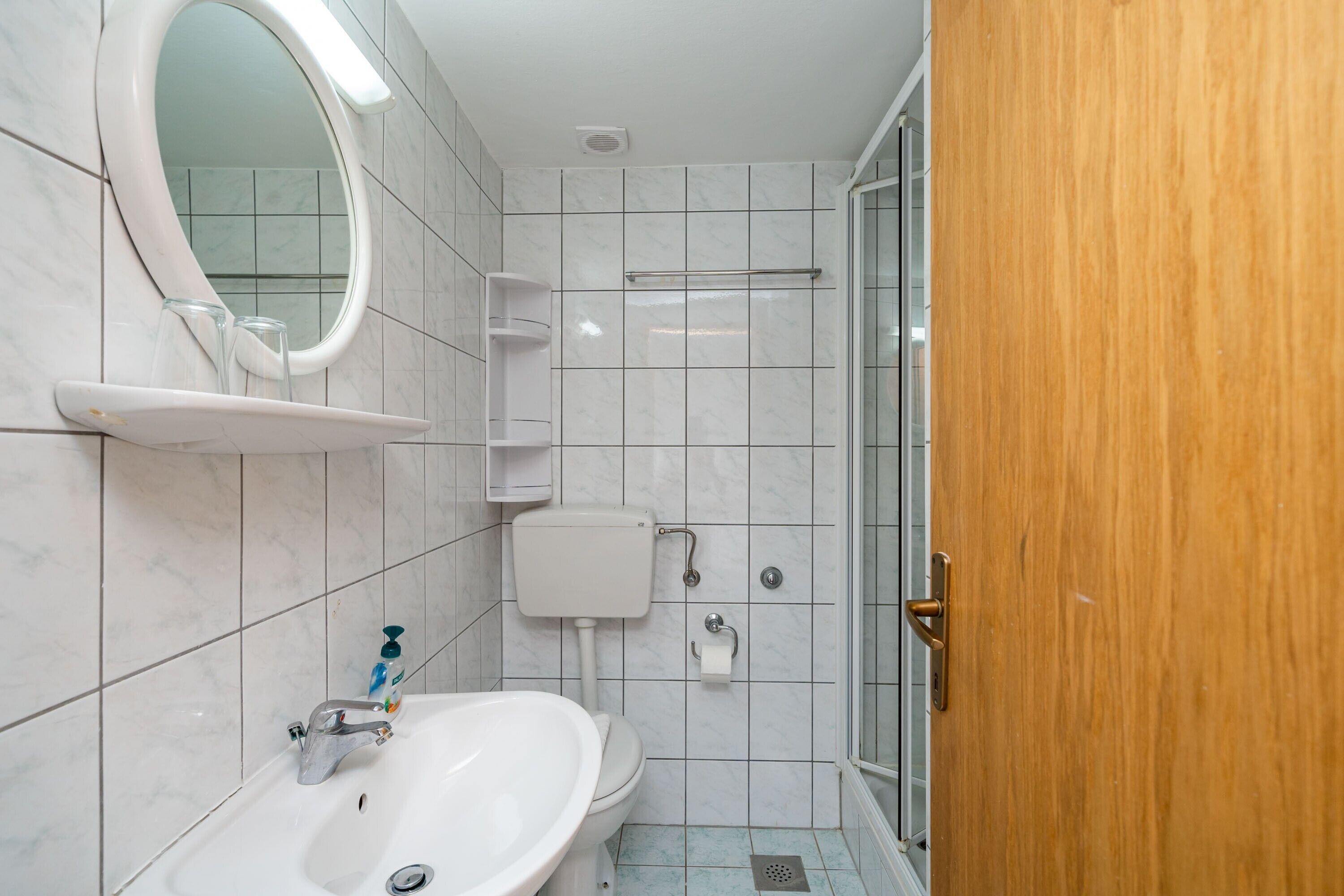 A bathroom with a sink, toilet, mirror, and shower.