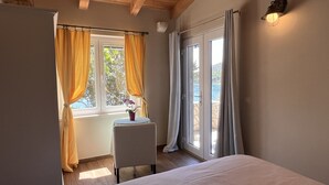 Une chambre avec un lit, une petite table sur laquelle est posé un vase, une fenêtre avec des rideaux et une vue sur une piscine.