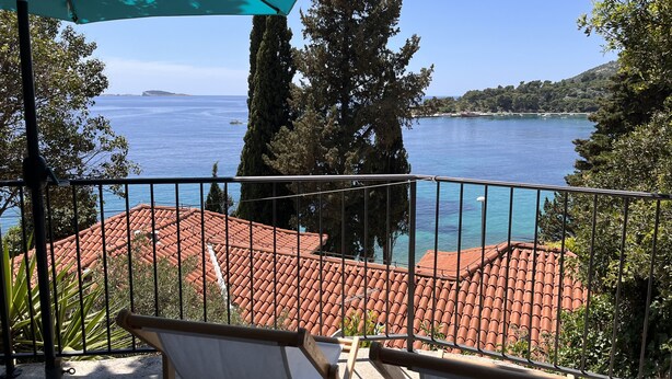 Un balcon avec vue sur la mer, un toit recouvert de tuiles et un grand parasol.