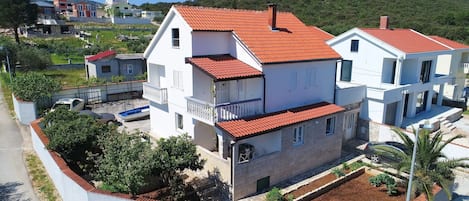 A two-story building with a red-tiled roof, a balcony, and a garden area with plants.