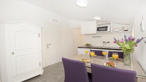 Une cuisine moderne avec des meubles blancs, une table à manger entourée de chaises violettes et un vase de fleurs.