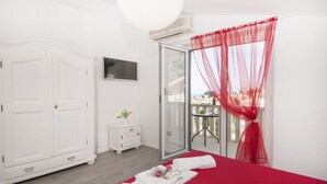 A bedroom with a bed, a wardrobe, a small table with a plant, and a balcony with a red curtain. - Apartments Villa Angela - One Bedroom Apartment with Terrace and Sea View (Baška Voda)