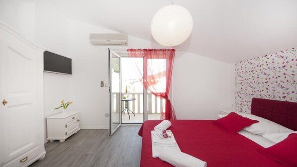 Une chambre avec une couvre-lit rouge, une commode blanche et un téléviseur fixé au mur.